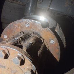 Road Service 24/7 - Zardzewiały element mechaniczny pojazdu z widocznymi śrubami i jasnym odbiciem światła na metalowej powierzchni, sugerujący naprawę lub konserwację.