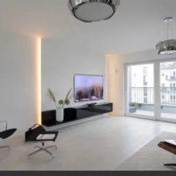 Minimalistyczny salon z białymi ścianami, podświetleniem LED w pionowej wnęce, czarnym stolikiem RTV, wiszącą lampą i wyjściem na balkon.