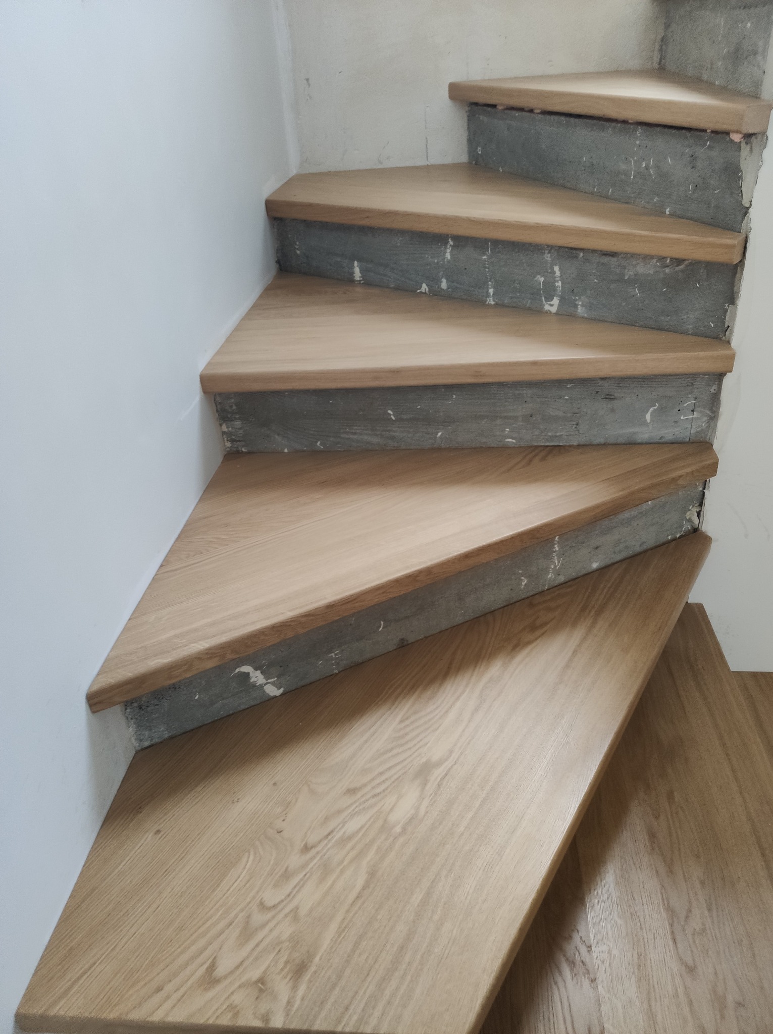 Drewniane schody zabiegowe z jasnego drewna, osadzone na betonowej konstrukcji, widoczne z góry w trakcie montażu. Minimalistyczny design.