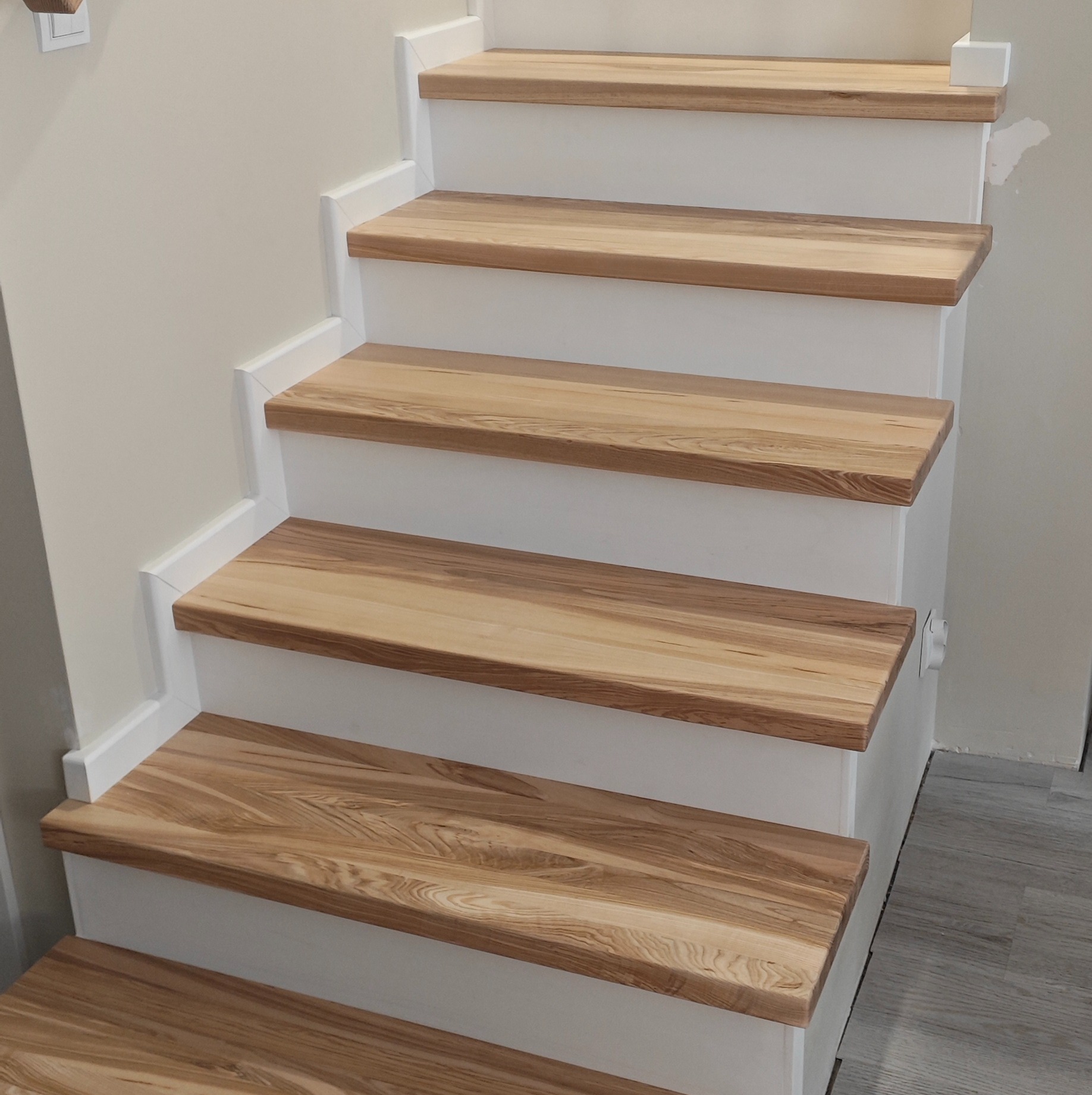 Detale wykończenia drewnianych schodów z białymi podstopnicami, widok z dołu, ukazujący naturalny rysunek drewna na stopniach i precyzję wykonania.