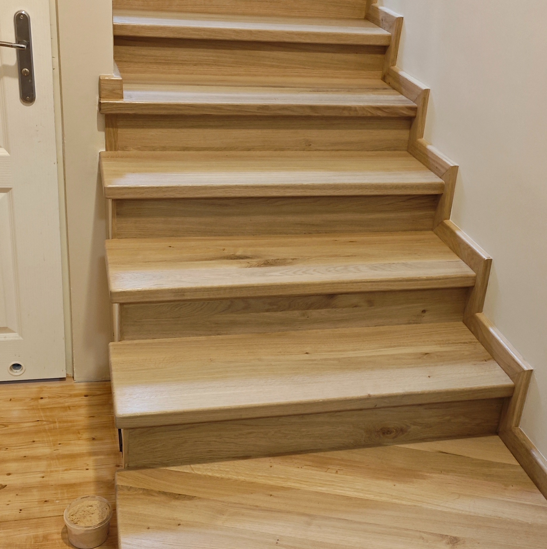 Drewniane schody z jasnego drewna w domu w Mrowino. Widoczne detale wykończenia stopni i podstopnic. Ujęcie z dołu, z boku, na pierwszym planie podłoga.