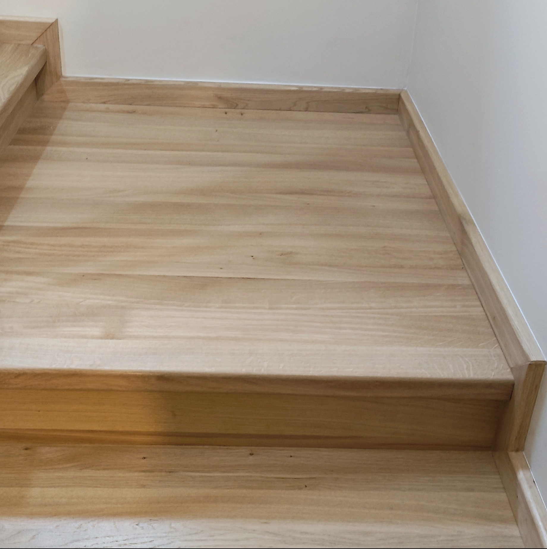 Jasne, drewniane schody z minimalistyczną listwą przypodłogową w odcieniu drewna, sfotografowane z dołu, ukazujące detale wykończenia.