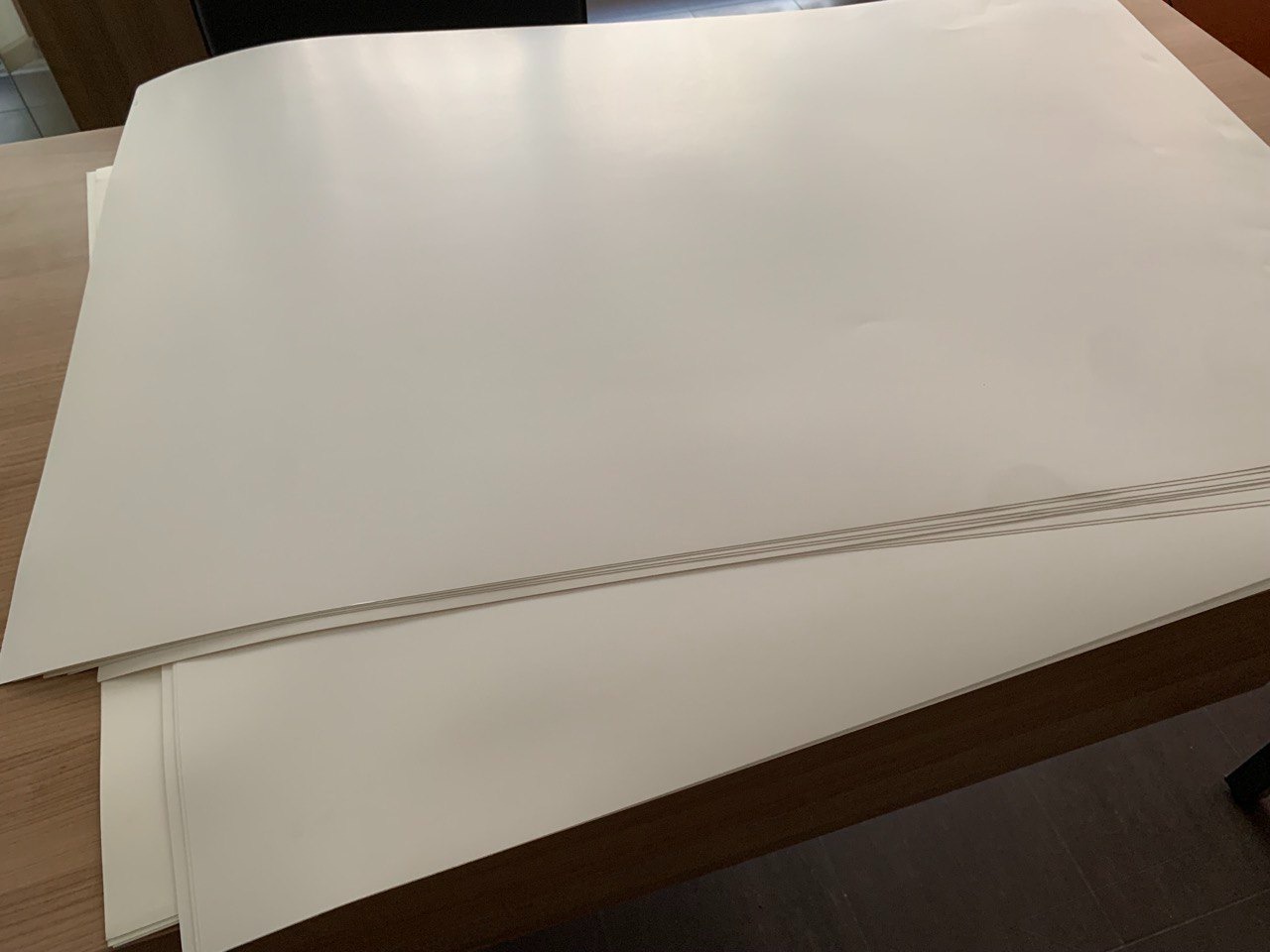 Stos arkuszy białego papieru na drewnianym stole, widoczne krawędzie i faktura papieru.