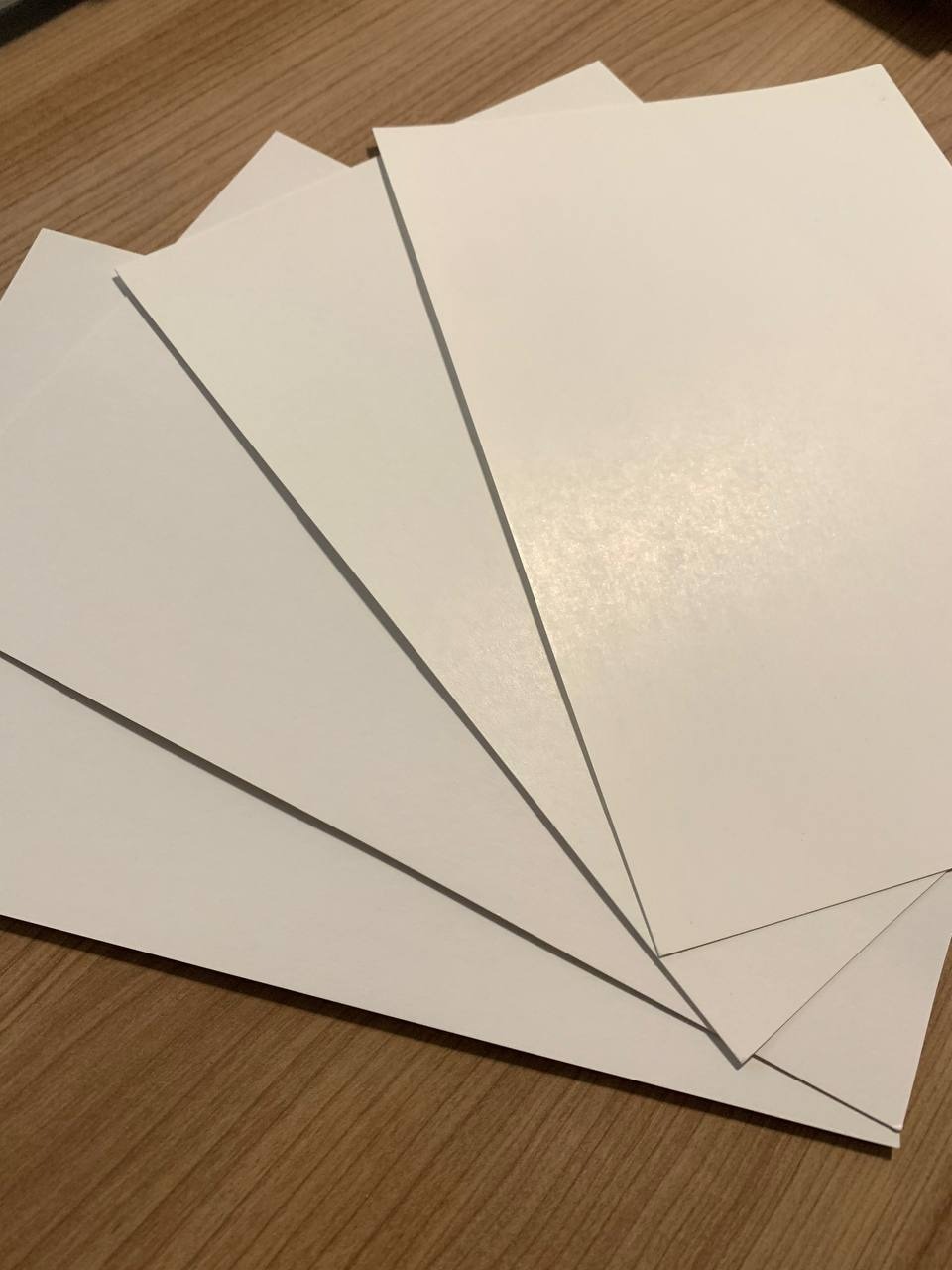 Stos białych kartek papieru ułożonych warstwowo na drewnianym blacie, widoczne cienie krawędzi.