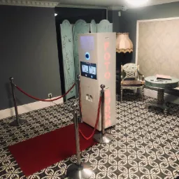 Foto budka z czerwonym sznurem odgradzającym na tle eleganckiego wnętrza z wzorzystą podłogą i dekoracyjnymi meblami.