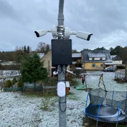 Dwie kamery monitoringu marki Dahua zamontowane na słupie, z widokiem na zasypany śniegiem ogród z trampoliną i domami w tle.