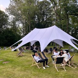 Fun Factory - Biały namiot gwiazda na zielonej trawie, otoczony leżakami i stolikami z ludźmi. Plenerowa impreza w otoczeniu drzew.