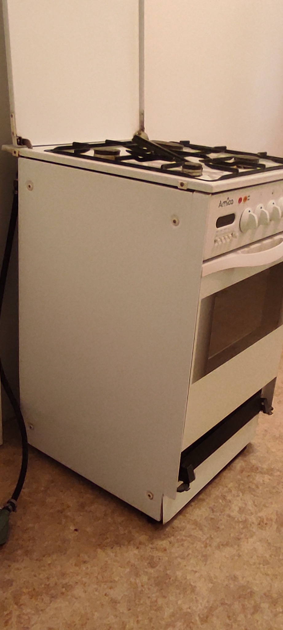 Biała kuchenka gazowa marki Amica z otwartą górną klapą, widoczne palniki i pokrętła, na podłodze imitującej terakotę.