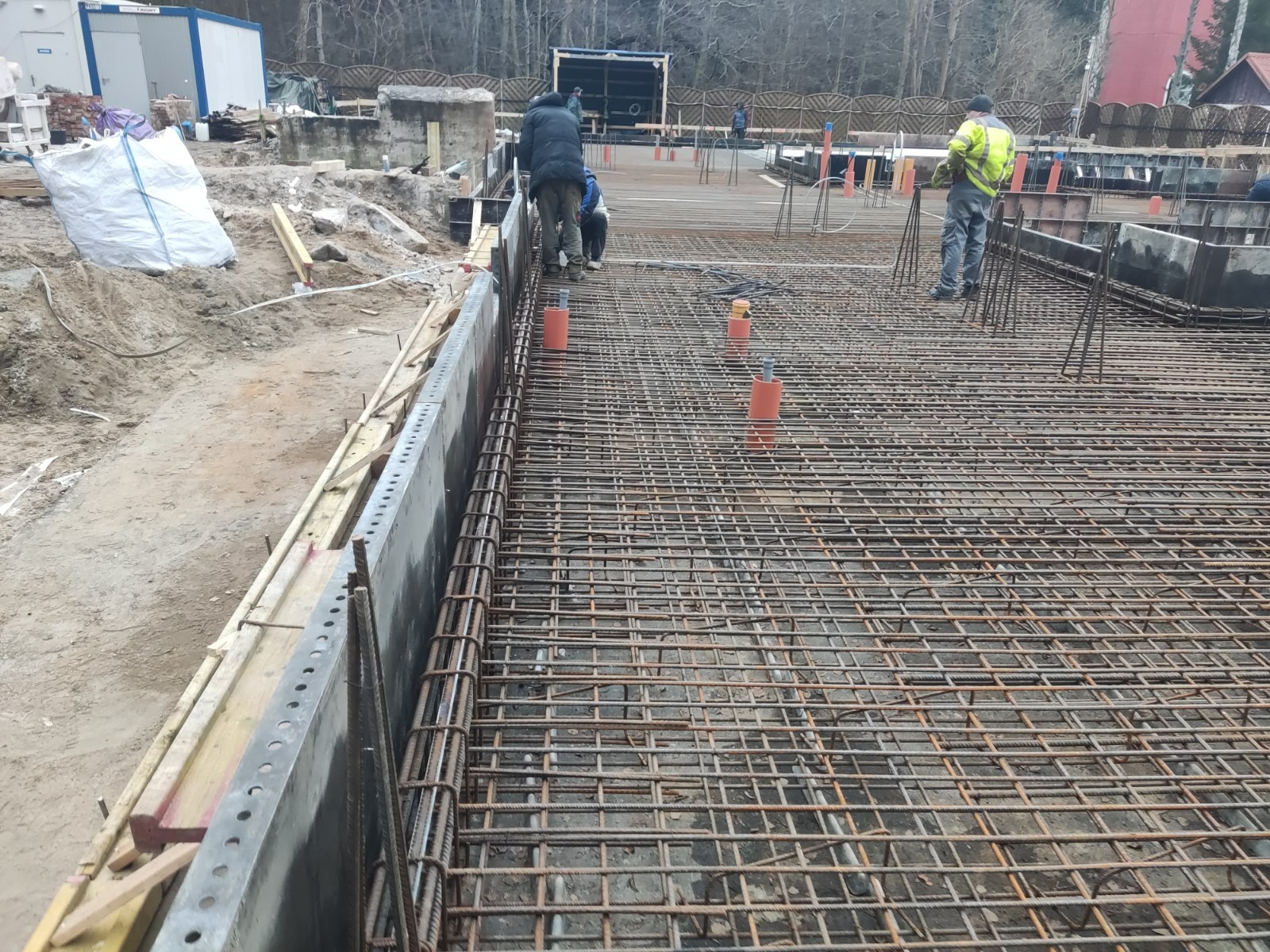 Zbrojenie płyty fundamentowej z widocznymi pracownikami i szalunkiem w trakcie budowy.