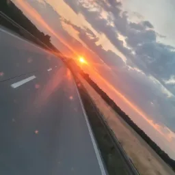 Autostrada w promieniach zachodzącego słońca, widok z perspektywy jadącego pojazdu, zarys lasu w oddali, delikatne rozmycie obrazu.