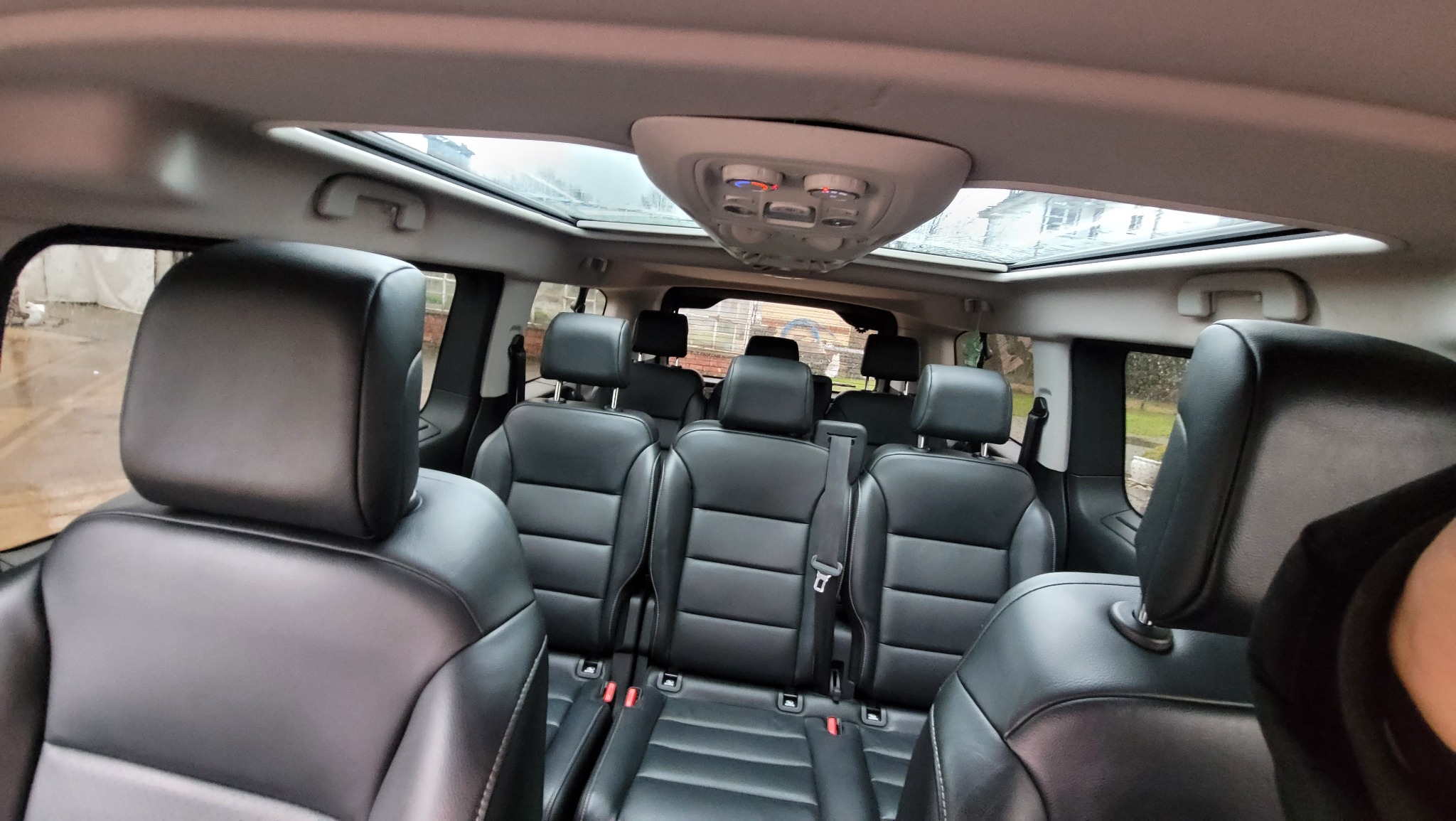 Wnętrze przestronnego busa z czarnymi skórzanymi siedzeniami i panoramicznym oknem dachowym, widok z perspektywy pasażera.