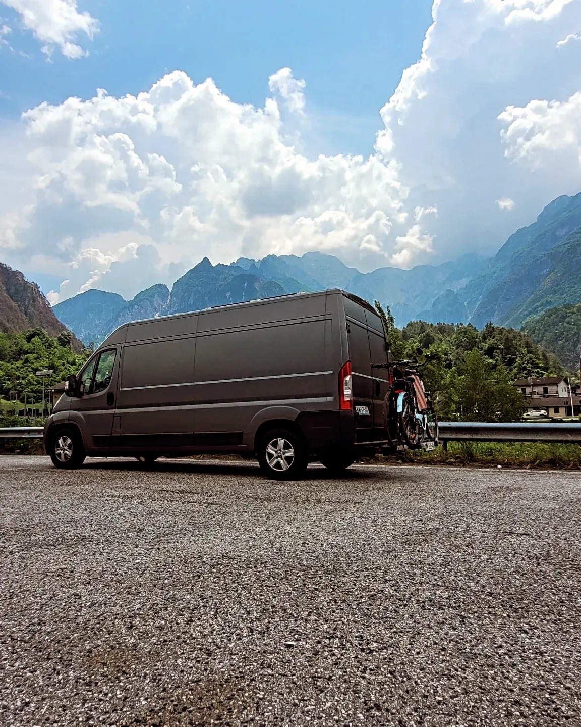 Szary bus zaparkowany na tle górskiego krajobrazu z rowerami zamontowanymi z tyłu.