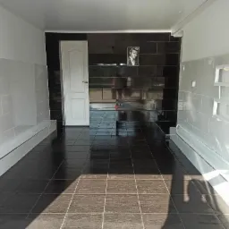 Wykończona łazienka z czarno-białymi płytkami, czarną podłogą i portretem na ścianie, widok na otwarte drzwi.