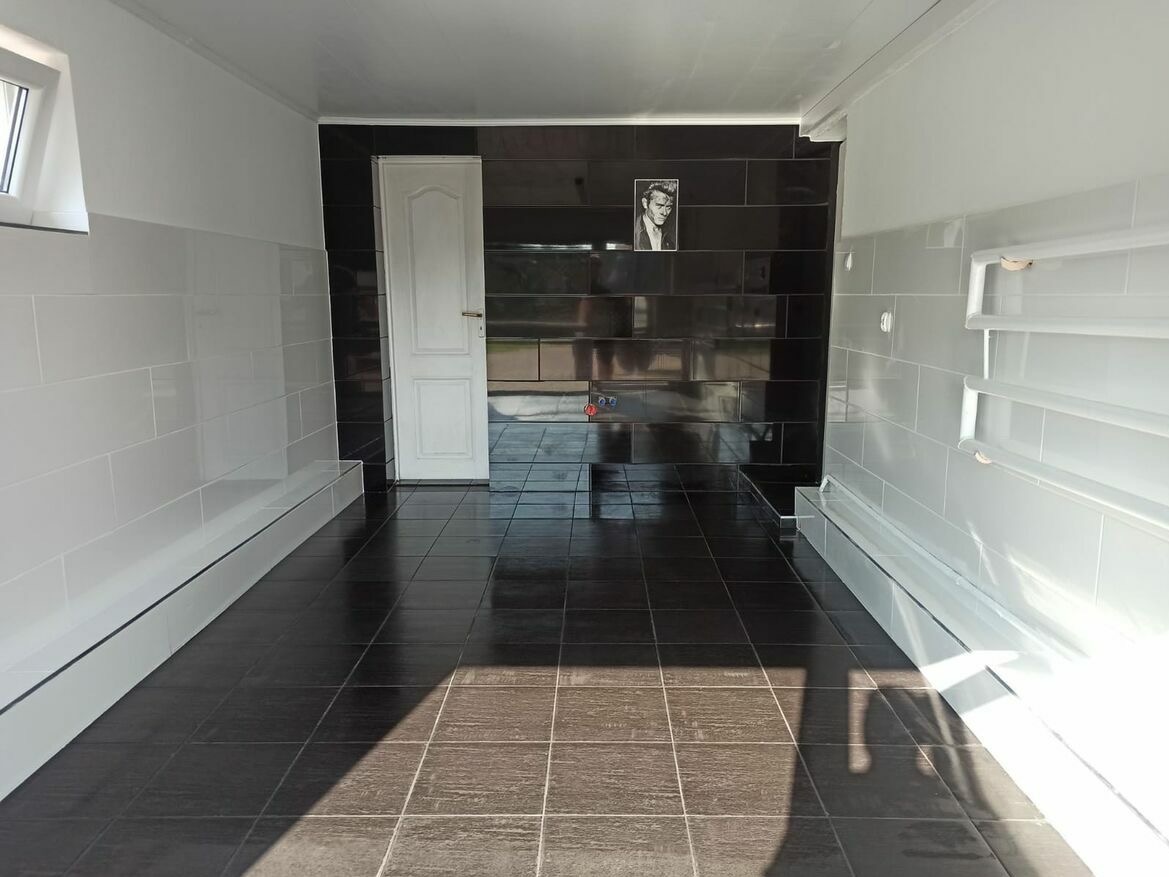 Wykończona łazienka z czarno-białymi płytkami, czarną podłogą i portretem na ścianie, widok na otwarte drzwi.