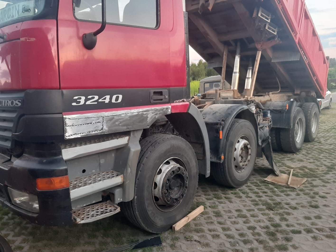Czerwona wywrotka Mercedes Actros 3240 z podniesioną skrzynią, widoczne naprawy blacharskie na kabinie, nierówna powierzchnia po spawaniu.