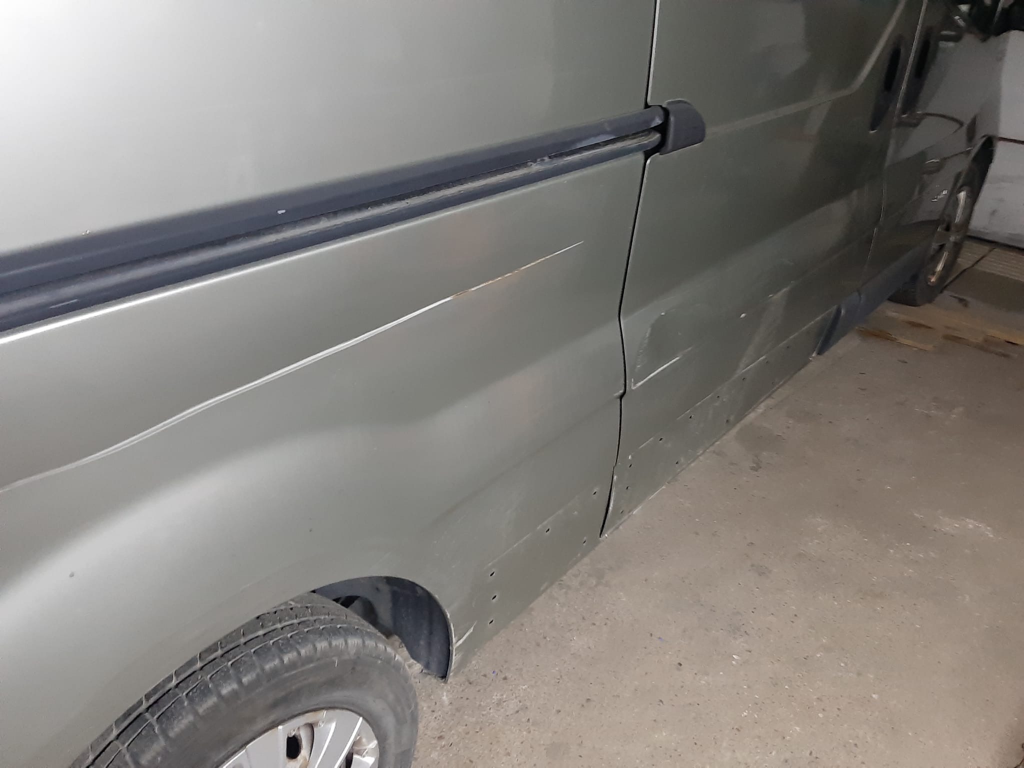 Bok samochodu dostawczego koloru khaki z widocznymi wgnieceniami, rysami i śladami po naprawie blacharskiej, widoczne otwory po spawaniu.