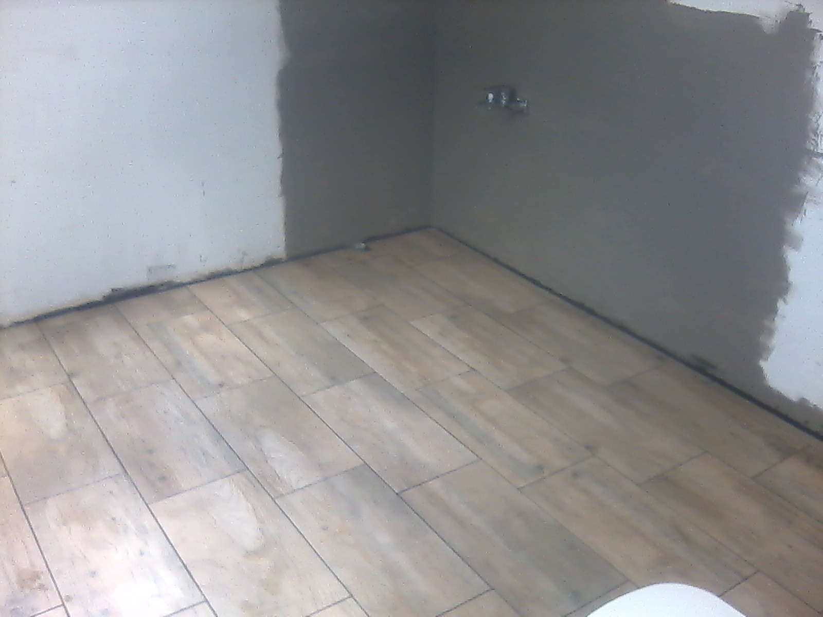 Podłoga wyłożona płytkami imitującymi drewno, świeżo położona zaprawa na ścianach, widoczne niedociągnięcia przy krawędziach.