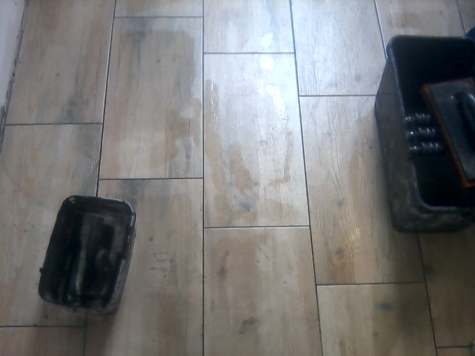 Ułożone płytki podłogowe imitujące drewno, z widocznymi dwoma pojemnikami z narzędziami do fugowania.