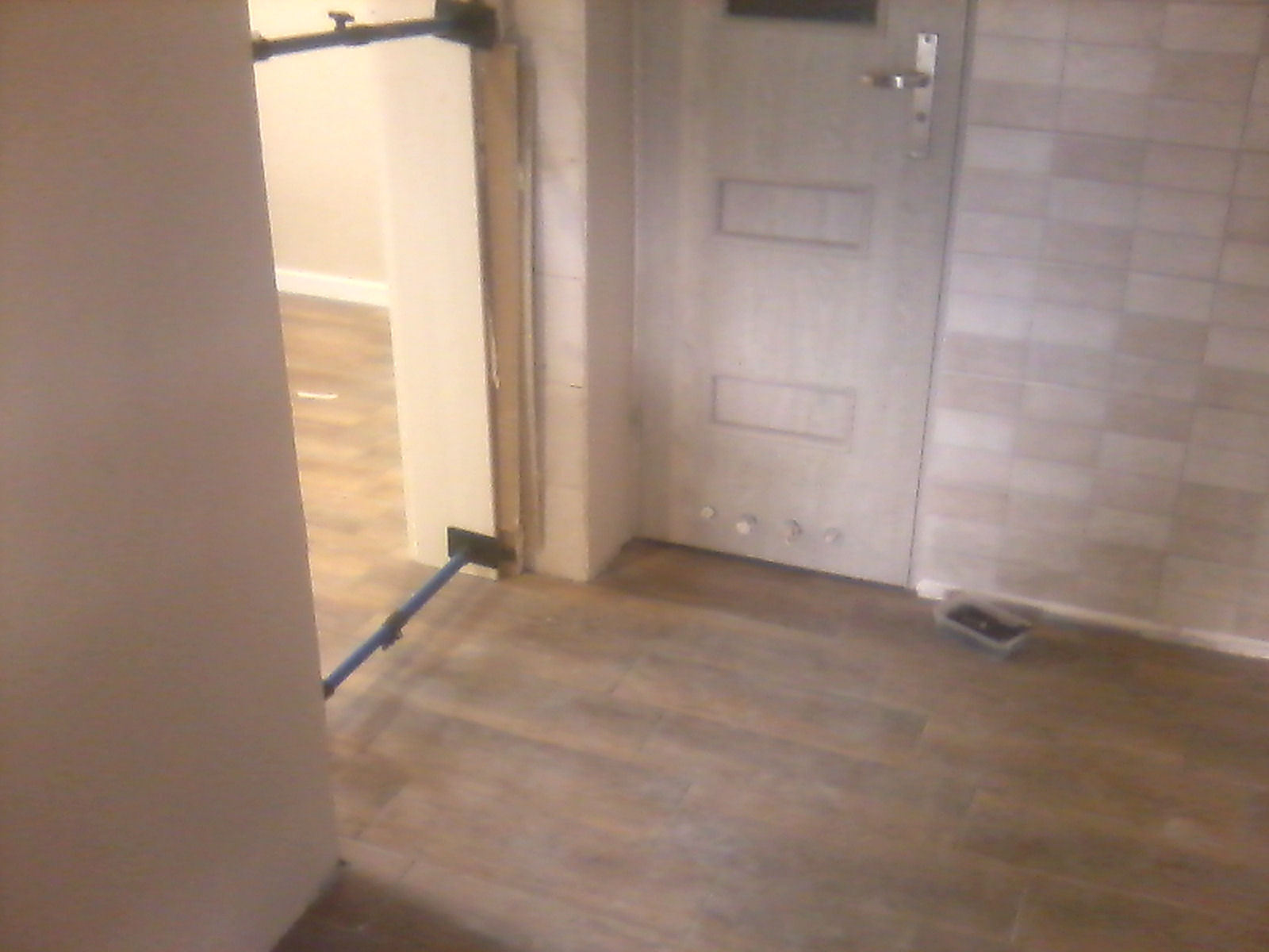 Ułożona podłoga z paneli imitujących drewno w przedpokoju, częściowo widoczna ściana wyłożona płytkami ceramicznymi, narzędzie do układania paneli przy ścianie.