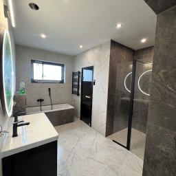 Brat-bud - Nowoczesna łazienka z marmurową podłogą i ścianami, czarną armaturą, kabiną prysznicową typu walk-in i podświetlanym lustrem. Minimalistyczny design z akcentami czerni.