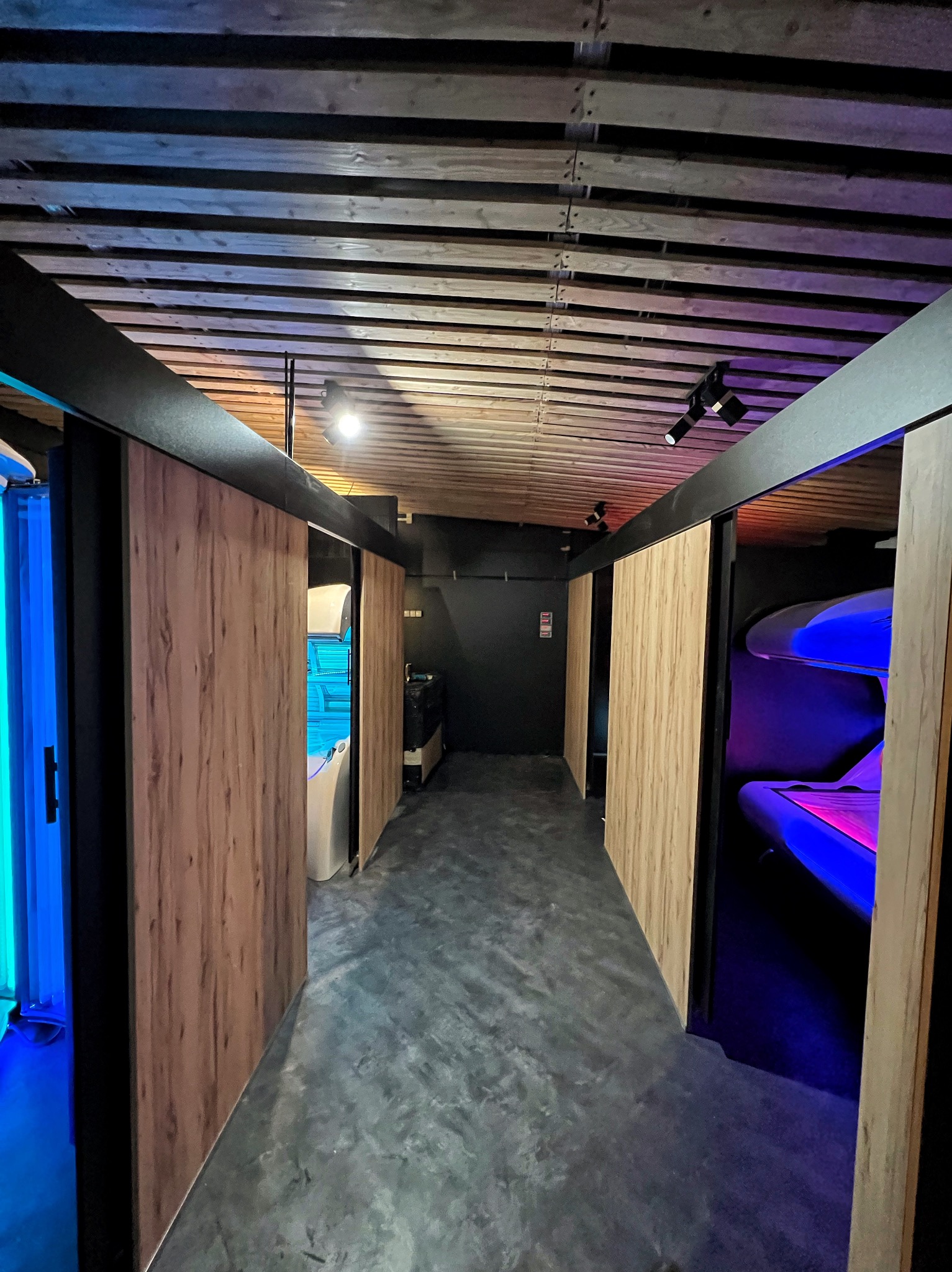 Nowoczesne wnętrze salonu solarium z kabinami opalającymi, drewnianymi panelami i intensywnym, kolorowym oświetleniem LED.