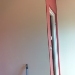 MIKO Perfekt - Świeżo pomalowane ściany w odcieniach beżu i różu w mieszkaniu w Pruszkowie, widoczna futryna drzwiowa w kolorze różowym i fragment narzędzia malarskiego przy ścianie.