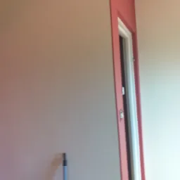 Świeżo pomalowane ściany w odcieniach beżu i różu w mieszkaniu w Pruszkowie, widoczna futryna drzwiowa w kolorze różowym i fragment narzędzia malarskiego przy ścianie.