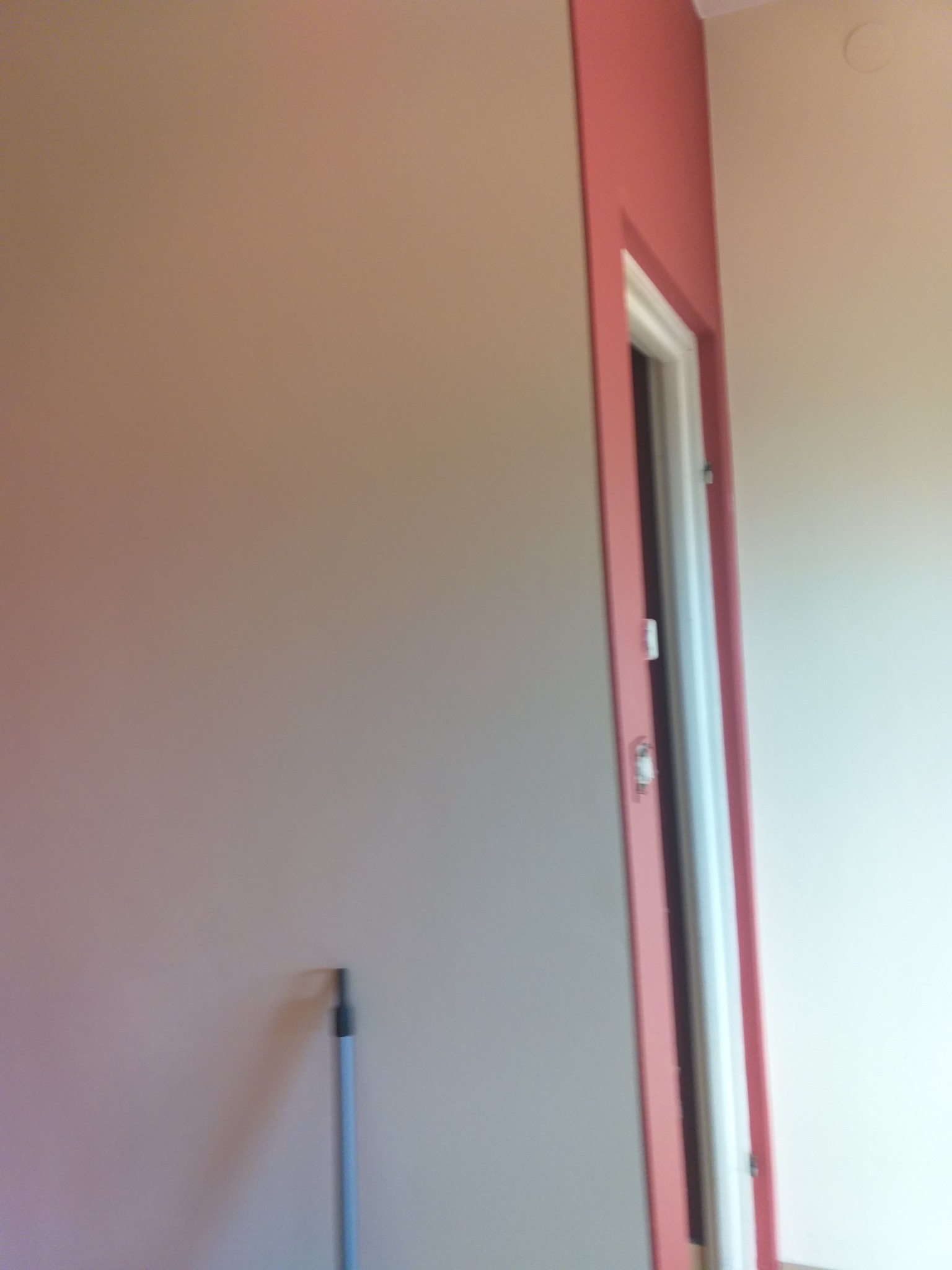 Świeżo pomalowane ściany w odcieniach beżu i różu w mieszkaniu w Pruszkowie, widoczna futryna drzwiowa w kolorze różowym i fragment narzędzia malarskiego przy ścianie.