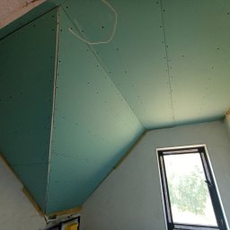 Piter-Bud Piotr Papiernik - Poddasze z oknem dachowym, wykończone płytami gipsowo-kartonowymi w kolorze zielonym, widoczne łączenia i wkręty. Ocieplenie widoczne w szczelinach.