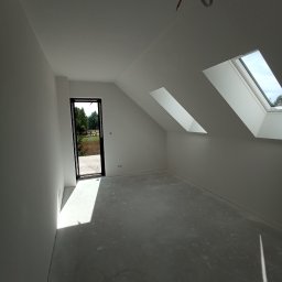 Piter-Bud Piotr Papiernik - Jasne poddasze po szpachlowaniu i malowaniu na biało, z oknami dachowymi i otwartym wyjściem na zewnątrz. Widoczne ślady po pracach na podłodze.