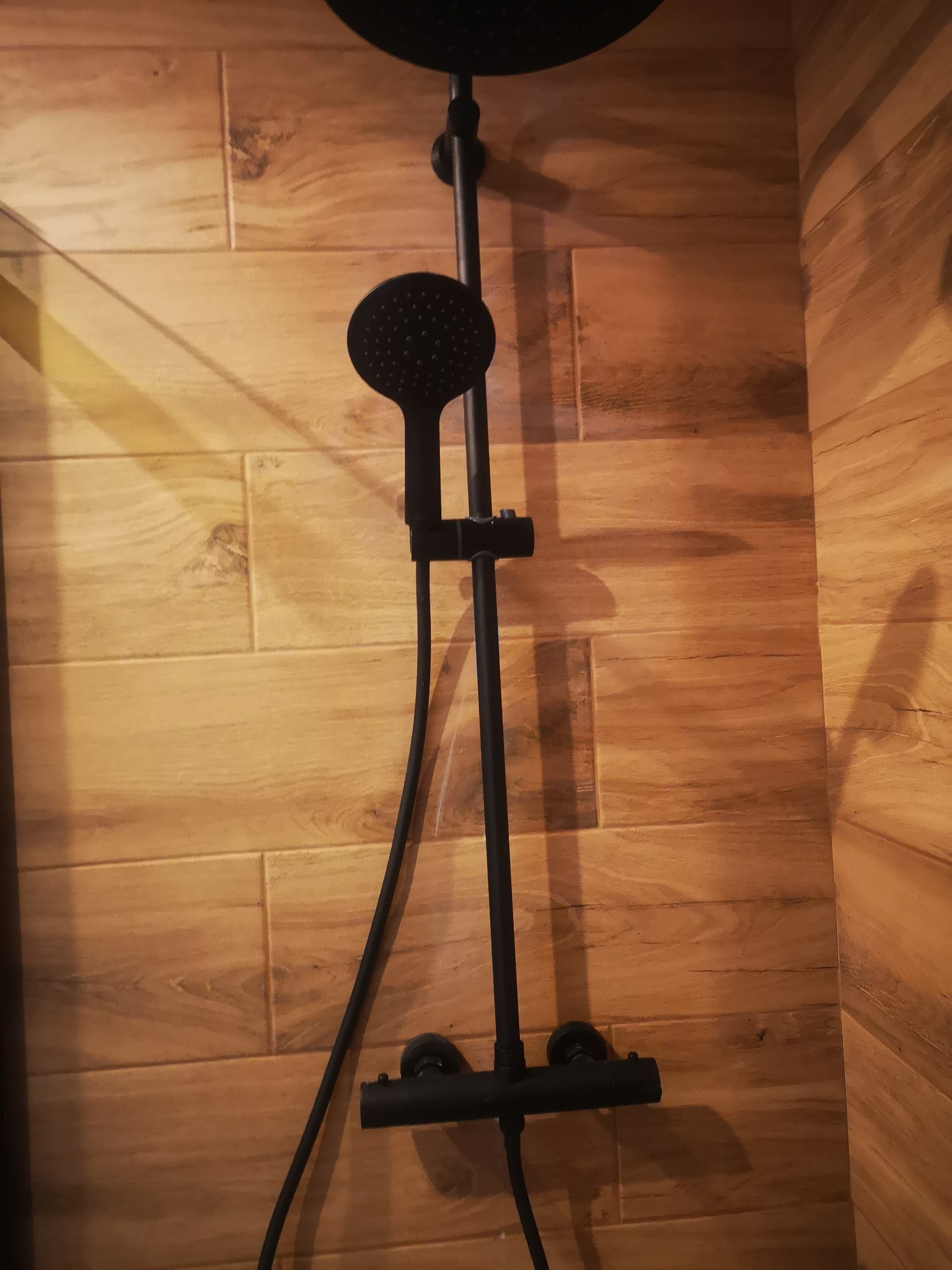 Czarny, nowoczesny zestaw natryskowy zamontowany na ścianie wyłożonej płytkami imitującymi drewno w łazience.