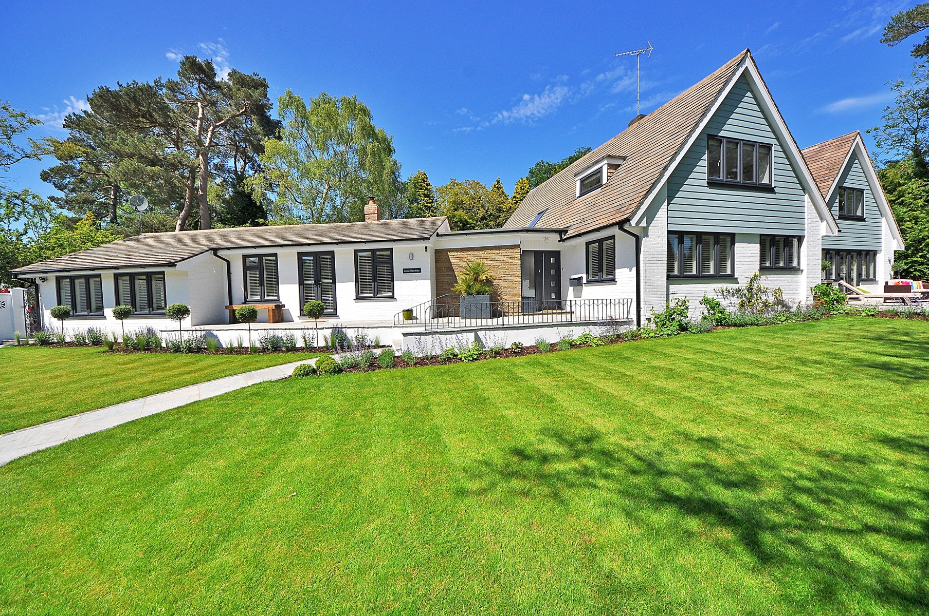 Elegancki dom jednorodzinny z białej cegły z ciemnymi okiennicami i zadbanym trawnikiem, widok z perspektywy trawnika w słoneczny dzień.