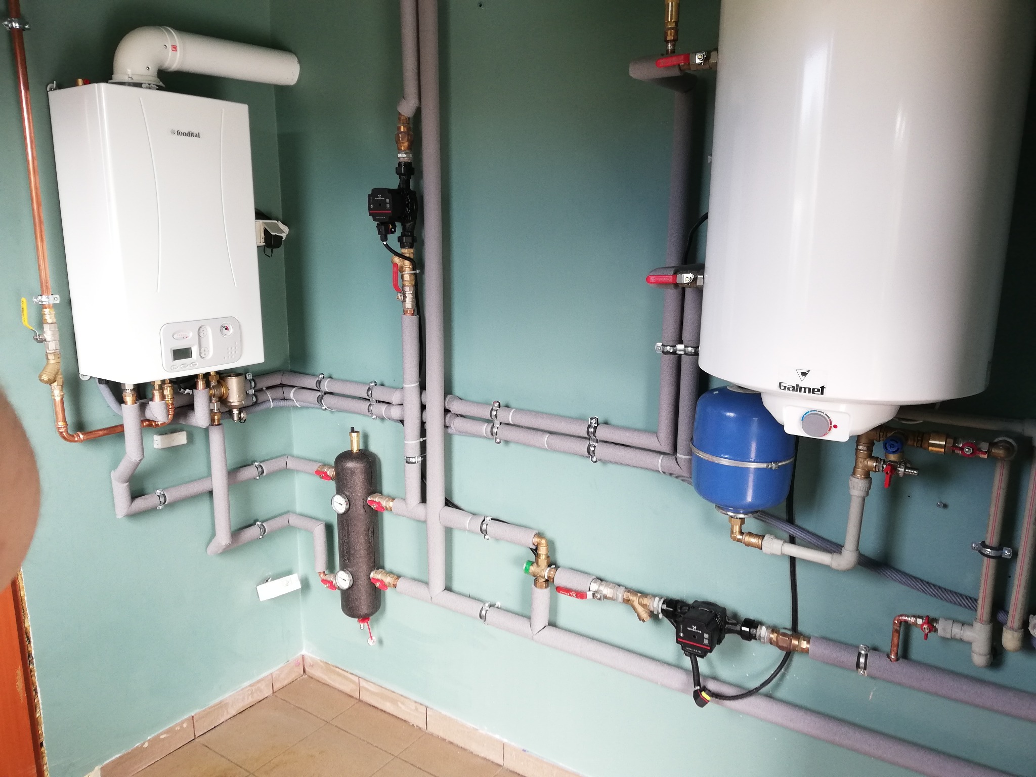 Złożona instalacja centralnego ogrzewania z piecem Fondital i zasobnikiem Galmet w Toruniu, z rurami zaizolowanymi szarą pianką i licznymi zaworami.