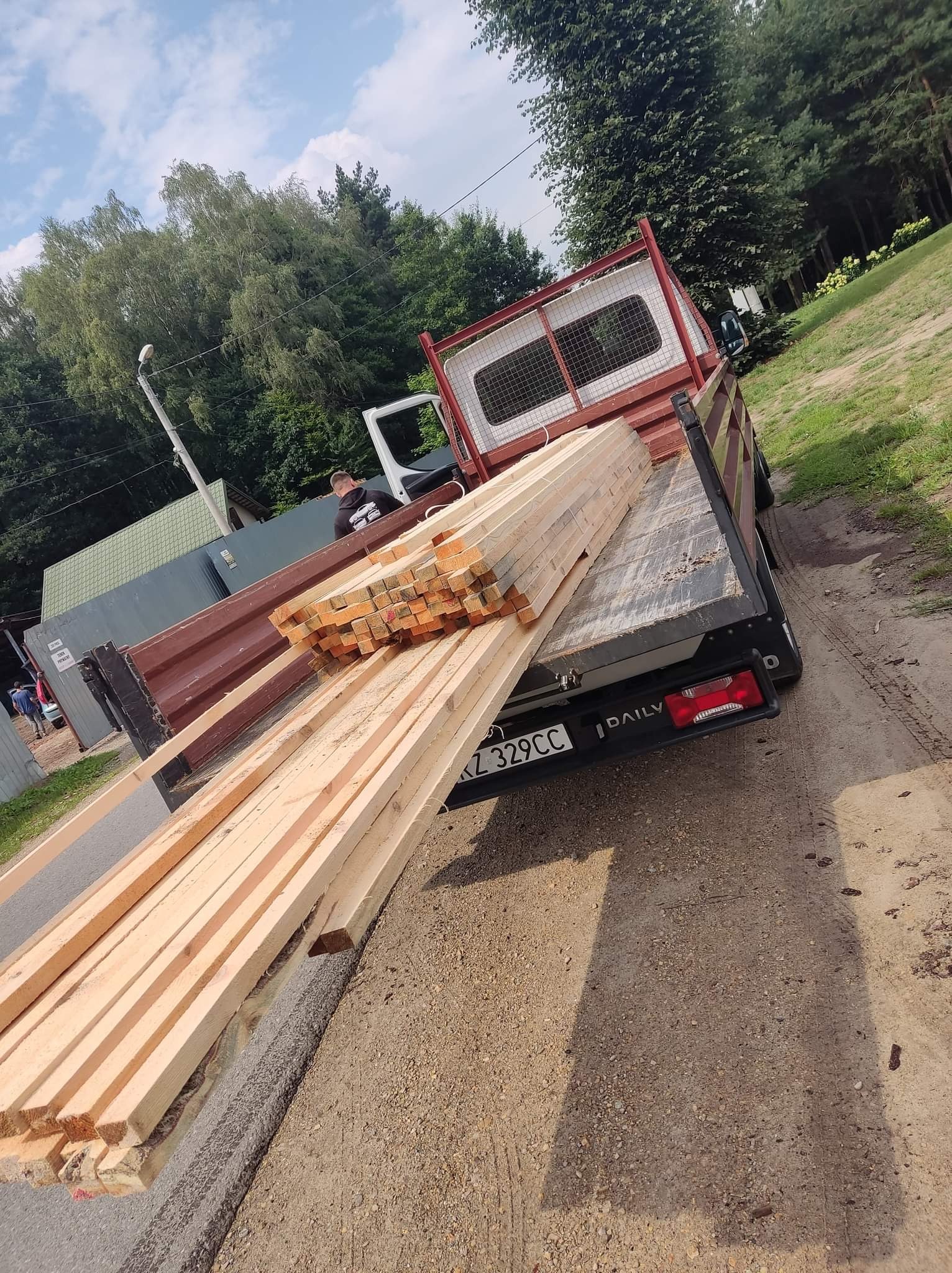 Ciężarówka z ładunkiem świeżo przetartego drewna, widoczne deski ułożone warstwami, w tle zieleń drzew.