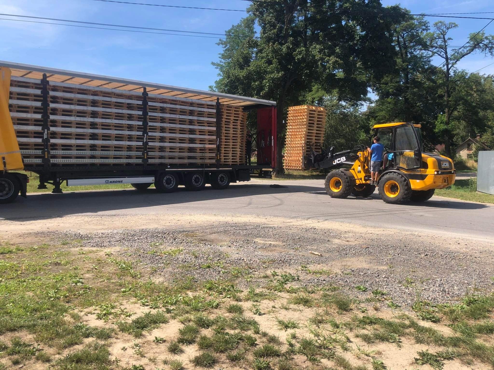 Załadunek palet z ciężarówki za pomocą ładowarki JCB na zewnątrz, widok z boku.