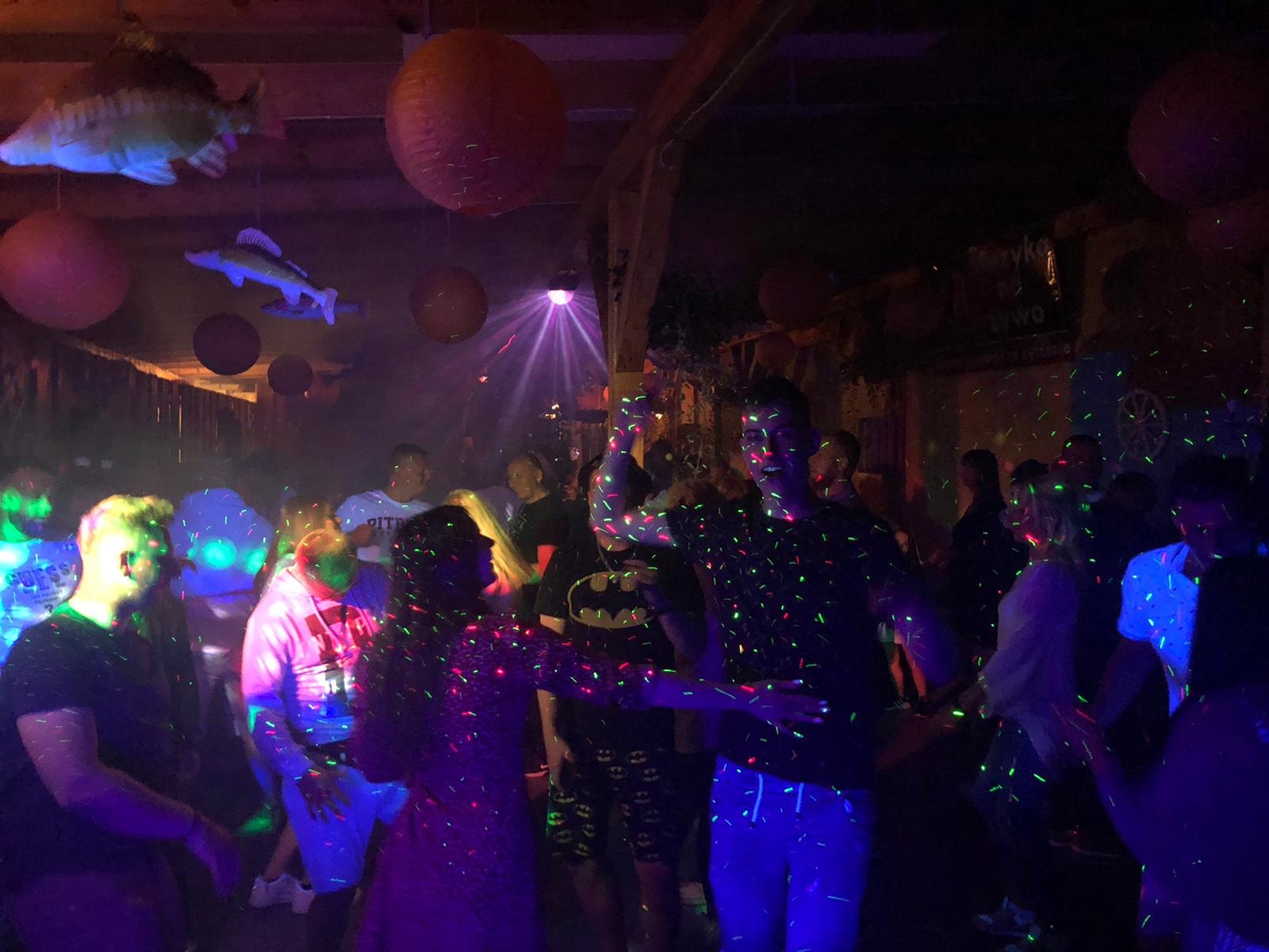 Roztańczony tłum w dyskotekowym oświetleniu, dekoracje z papierowych lampionów i ryb podwieszonych pod sufitem.