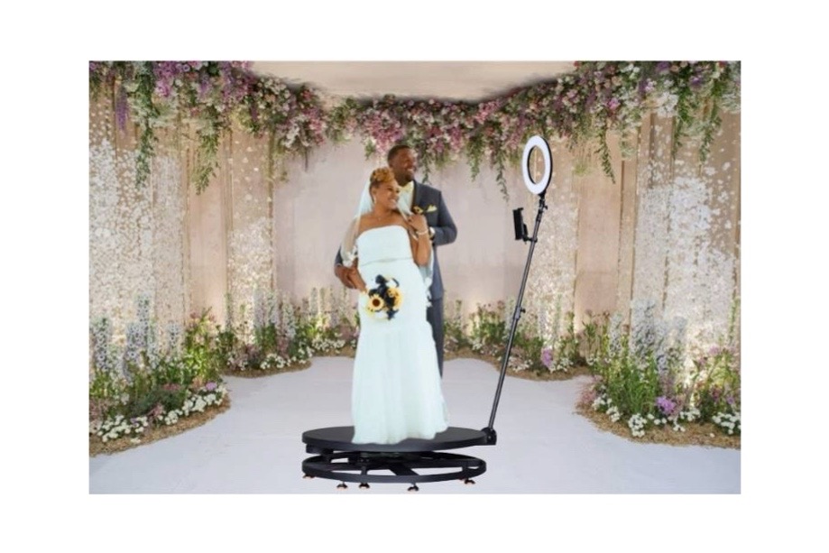 Para młoda pozuje na platformie obrotowej fotobudki 360 stopni z lampą pierścieniową podczas wesela, w tle dekoracja kwiatowa.