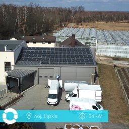 Passive Instal Sp. z o.o. - Marcin Gorajek - Widok z góry na budynek z panelami słonecznymi na dachu, kilka dostawczych samochodów zaparkowanych przed budynkiem, w tle szklarnie i las.