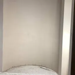 Świeżo otynkowana ściana z zaokrąglonym narożnikiem u podłogi, widoczne ślady po pracach na podłodze i niedokończone wykończenie sufitu.