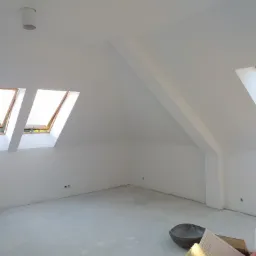 Poddasze z oknami dachowymi po nałożeniu gładzi, widoczne narzędzia i materiały budowlane na podłodze.