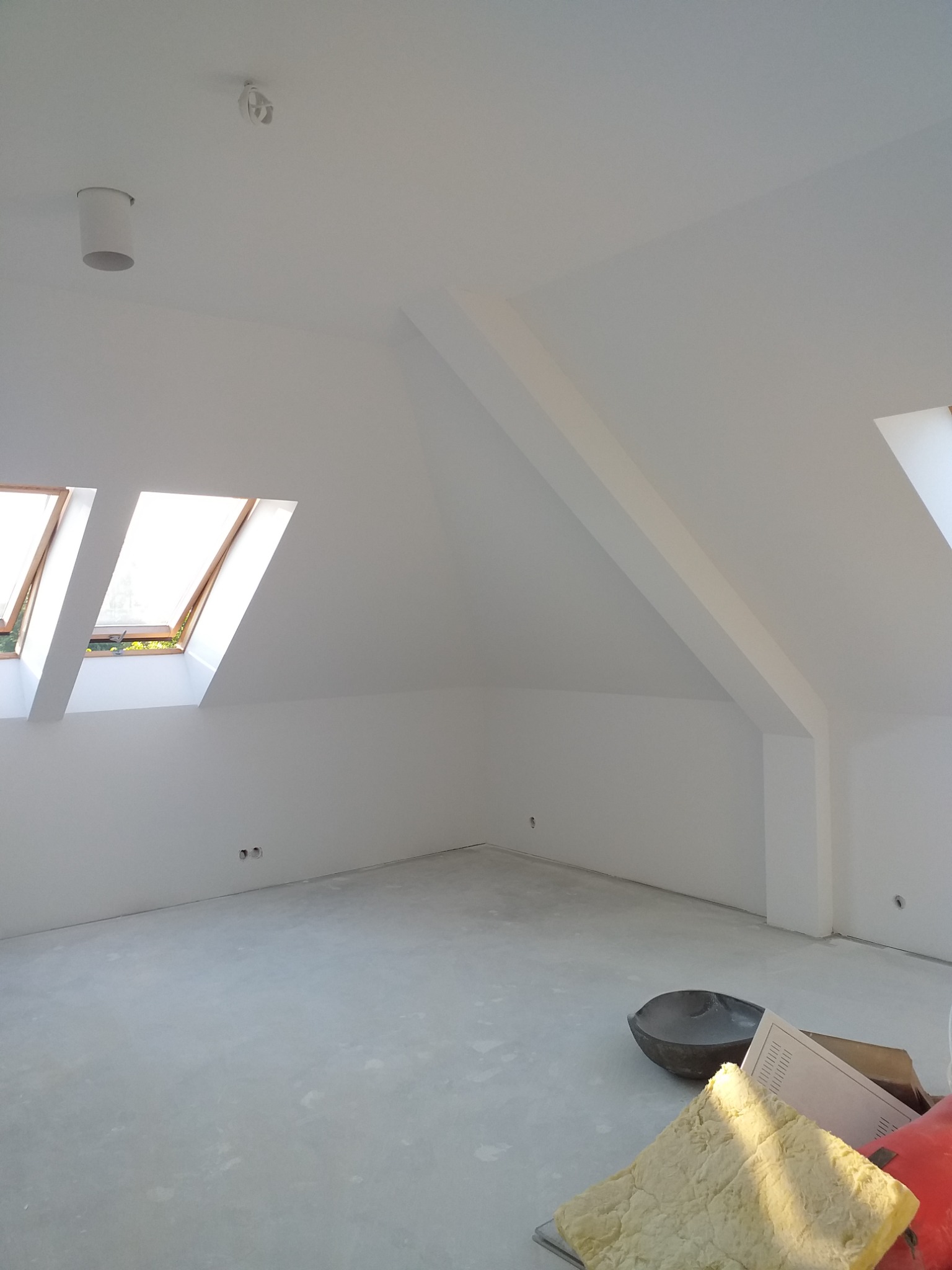 Poddasze z oknami dachowymi po nałożeniu gładzi, widoczne narzędzia i materiały budowlane na podłodze.