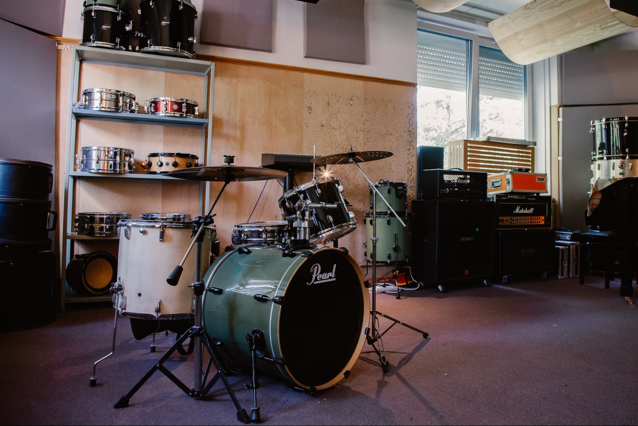 Zielony zestaw perkusyjny Pearl w profesjonalnym studiu nagrań, z półkami pełnymi werbli i wzmacniaczami w tle. Akustyczne panele na ścianach.