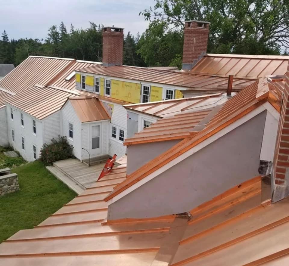 Widok z góry na budynek z nowym, miedzianym dachem z widocznymi kominami z cegły i rozłożoną czerwoną drabiną opartą o drewniany taras.