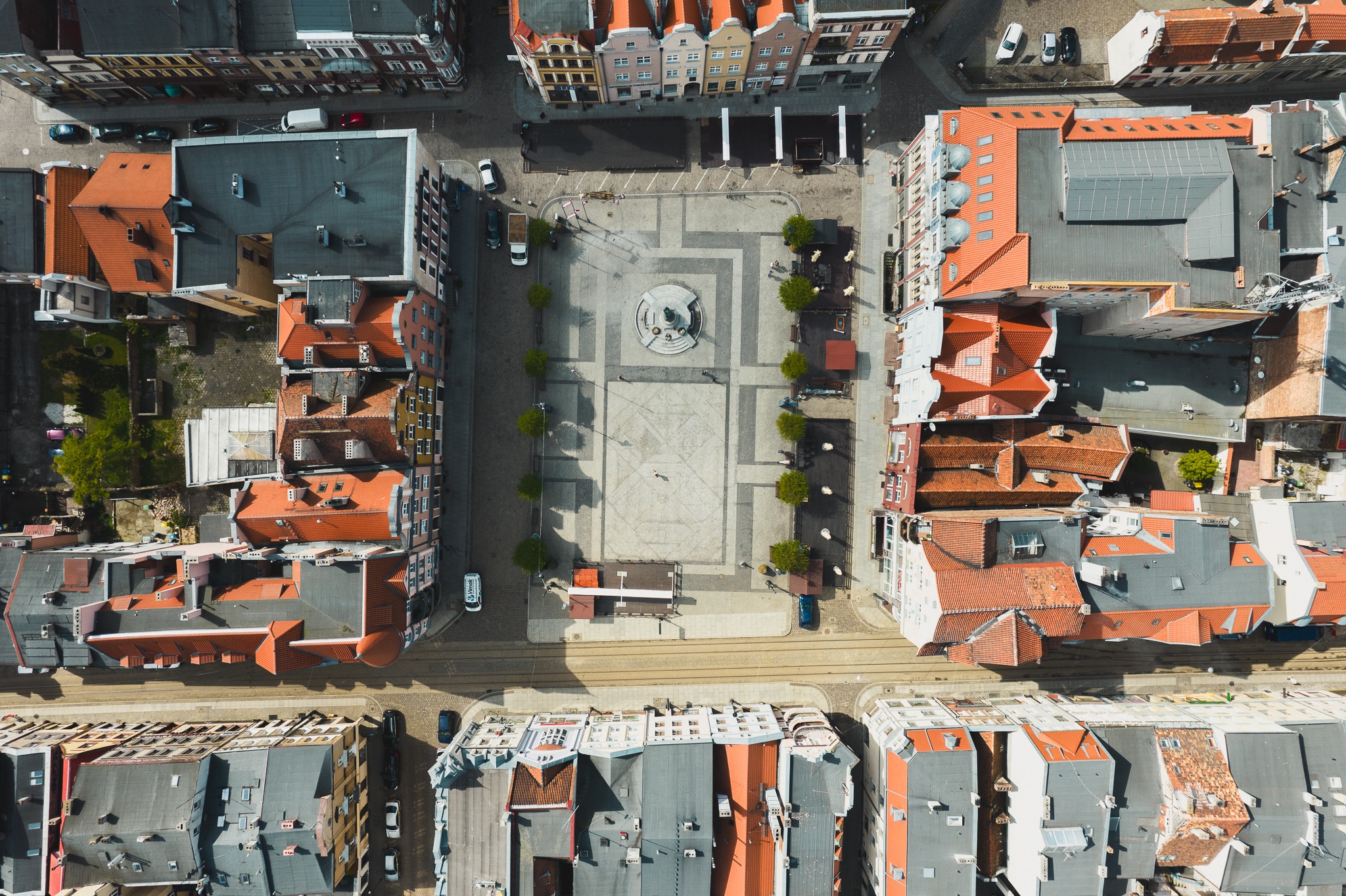 Widok z lotu ptaka na starówkę z centralnym placem, otoczonym kamienicami z czerwonymi dachami, drzewami i tramwajami.