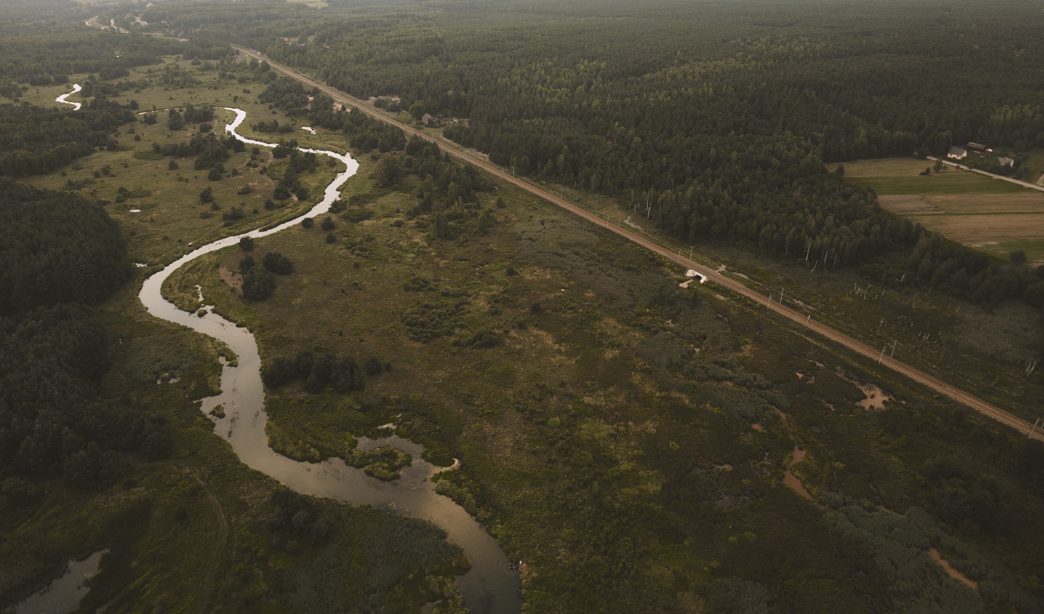 Widok z lotu ptaka na meandrującą rzekę przecinającą zielony krajobraz z lasami i linią kolejową w tle.