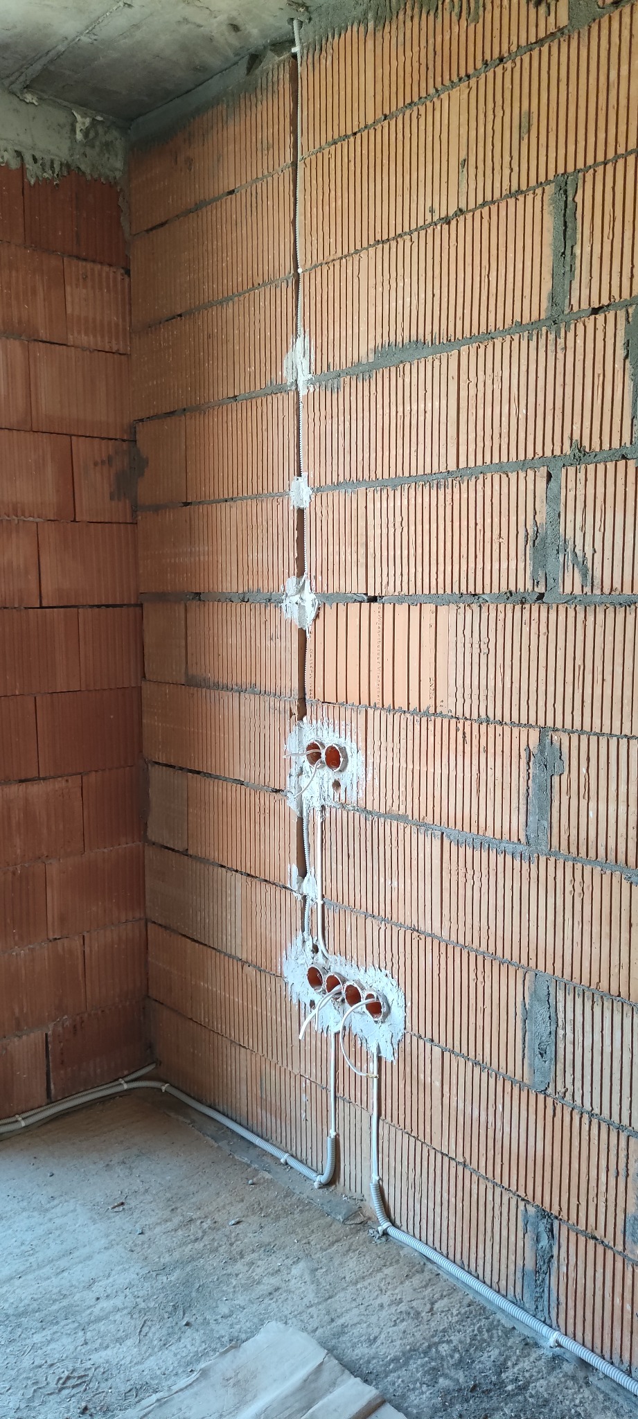 Instalacja elektryczna w surowym stanie: przewody w ścianie z czerwonej cegły, przygotowane otwory pod gniazdka zalane gipsem, widoczne kable.