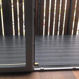 KarDes Karol Desecki - Nowoczesny balkon z szarą, kompozytową podłogą, drewnianą balustradą z pionowych desek i rozsuwanymi drzwiami balkonowymi.