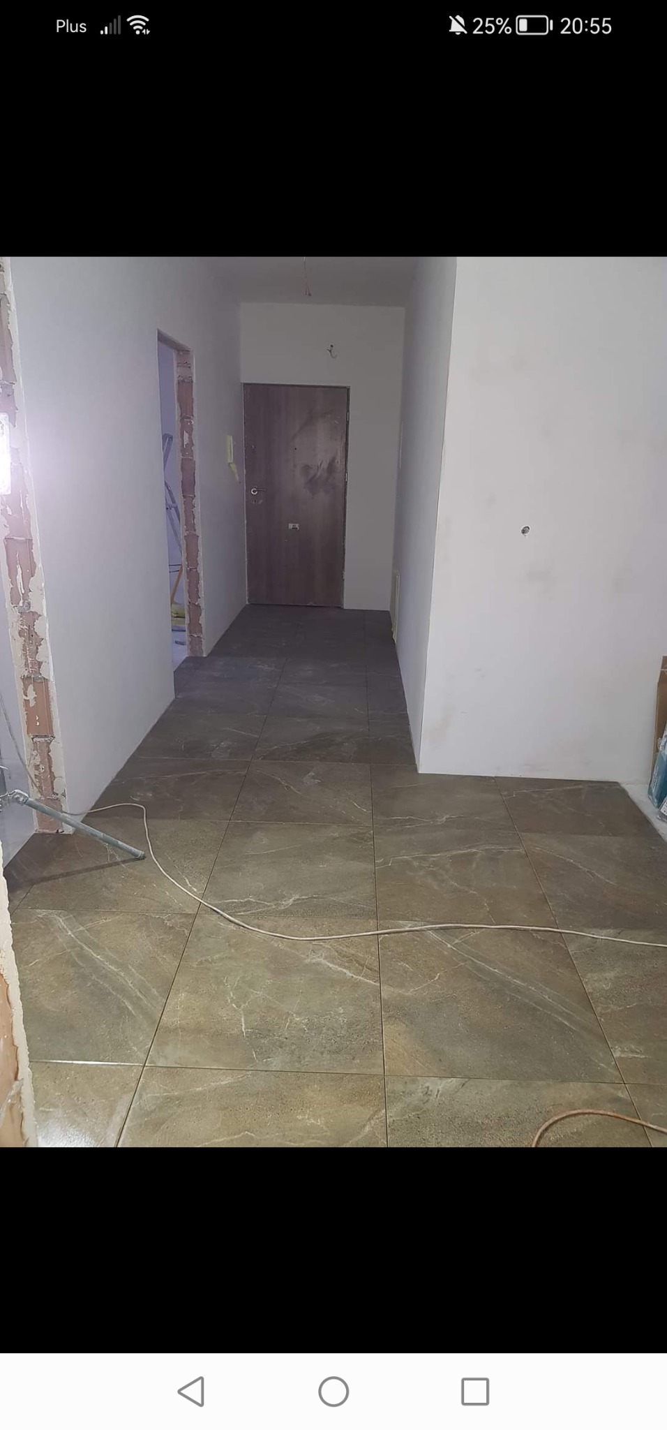 Ułożona podłoga z płytek imitujących kamień w korytarzu w trakcie remontu, widoczne niedokończone ściany i wystające kable.