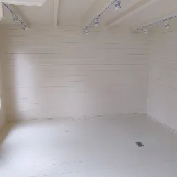 Wnętrze pomieszczenia wykończonego boazerią w jasnym odcieniu, z oknem i zamontowanym oświetleniem szynowym.