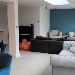 daz-build - Jasne, przestronne wnętrze domu z nowoczesnymi meblami, w tym szarą sofą chesterfield, czarnym pianinem i drewnianym stołem z aksamitnymi krzesłami, oświetlone naturalnym światłem przez duże okna...